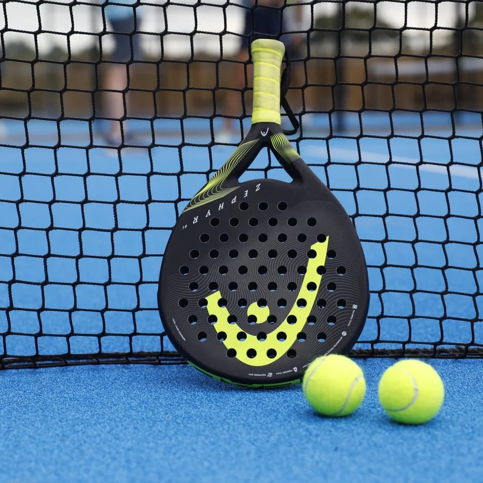 Padel racket and balls resting against the net on a blue sand-dressed padel court