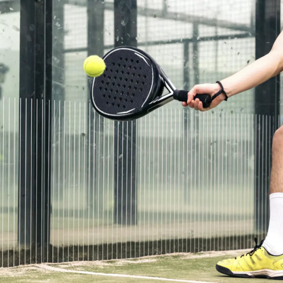 Padel player striking the ball beside the glass wall of an enclosed padel court