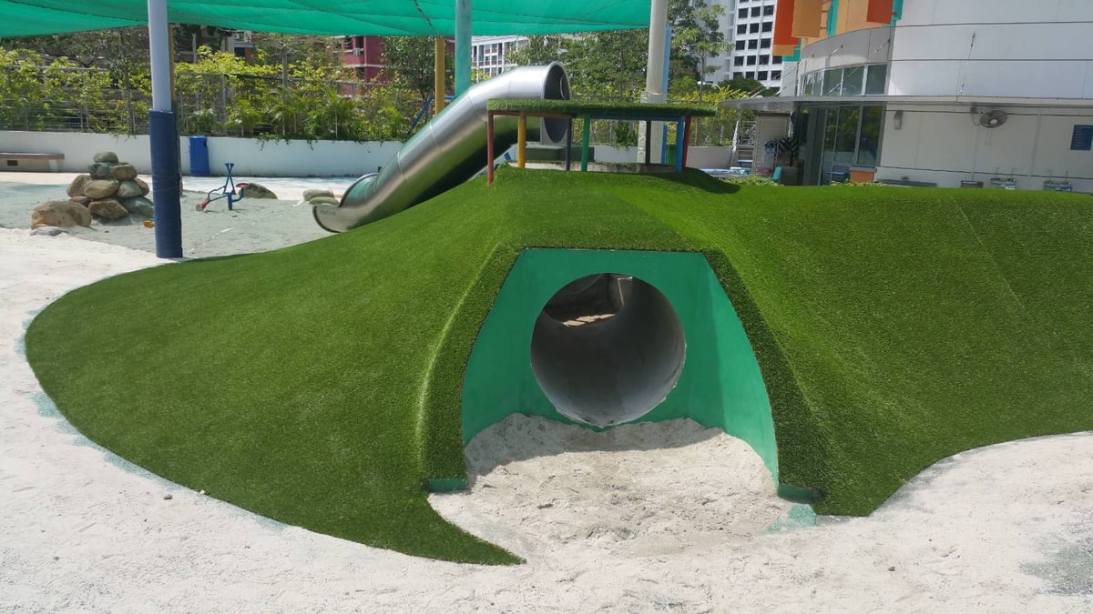 Artificial grass playground mound with a tunnel and slide over soft sand at United World College, Singapore